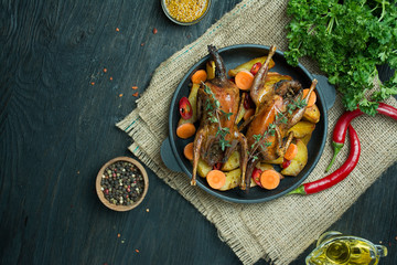 Baked quail with vegetables in a pan. Space for text. Dark background.