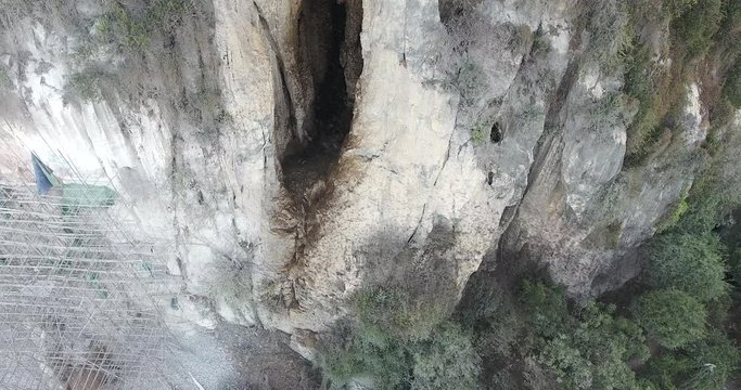 overhead drone shot of a stream of bats emerges from a hilltop cave