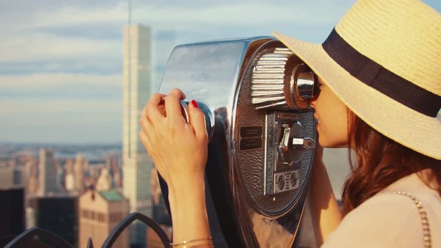 Young woman looking through binoculars at the city from above