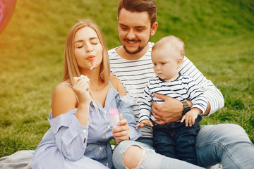 Fototapeta premium A young and beautiful blonde mother in a blue dress, along with her handsome man dressed in a white jacket, siting with her little son in the summer solar park