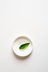 Means for skin care, rejuvenation and hydration of the face. Cream, moisturizing lotion on a white background with a green leaf. The concept of self-care and care for the skin