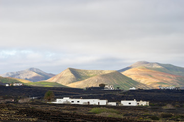 landscape with a black field, white house and volcano at background