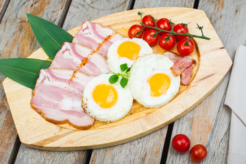 Tasty fried eggs with vegetables on a wooden plate.
