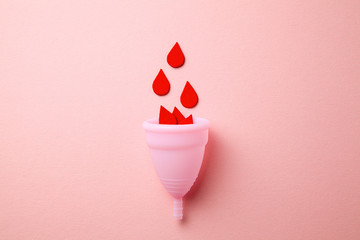 Silicone menstrual cup. Women's health and alternative hygiene. Cup with drops of blood on a pink background. - obrazy, fototapety, plakaty