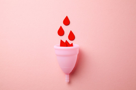Silicone menstrual cup. Women's health and alternative hygiene. Cup with drops of blood on a pink background.