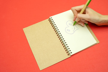 Hand of a girl who draws a heart in a notebook on a red background. Concept of Valentine's day, holiday