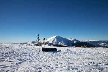 Tripod for photography camera, ski poles, snowboard on snow and snow-capped mountains
