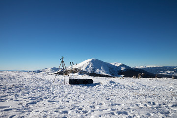 Obraz premium Tripod for photography camera, ski poles, snowboard on snow and snow-capped mountains
