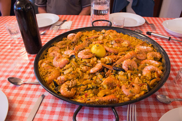 Seafood paella on checkered tablecloth. Delicious seafood meal. Mediterranean cuisine. Paella pan with king shrimps and bottle of wine. Tasty spanish dinner. Traditional mediterranean food.