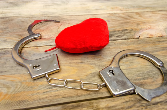 Handcuffs lie on a wooden background next to red heart. concept of crime, unrequited love, psychology