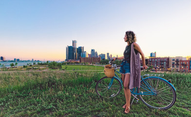 Young woman with bicycle with Detroit Skyline during sunset 