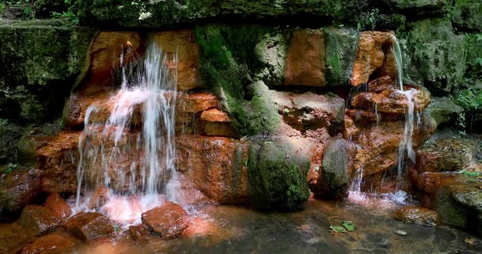 A natural flow of water gushes forth from the colorful orange yellow rocks of the Yellow Spring at Glen Helen Nature Preserve in Greene County, Ohio in this seamless video loop