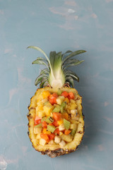 Tropical fruit salad in pineapple halves on a light blue background, Top view, vertical orientation