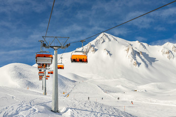 Ski lift ropeway on hilghland alpine mountain winter resort on bright sunny day. Ski chairlift cable way with people enjoy skiing and snowboarding.Banner panoramic wide view of downhill slopes