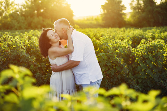 Aduld couple in a summer field. Handsome senior in a white shirt. Woman in a white dress