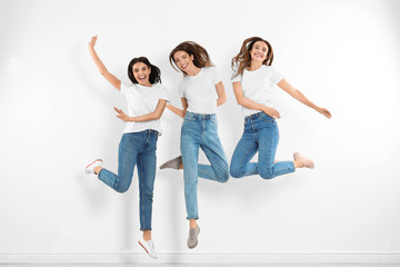 Obraz premium Group of young women in stylish jeans jumping near white wall
