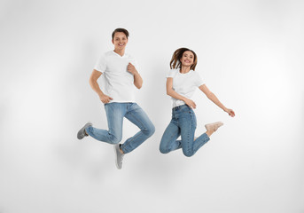 Fototapeta na wymiar Young couple in stylish jeans jumping near white wall