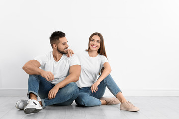 Young couple in stylish jeans sitting near white wall