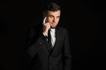 Handsome young businessman talking by mobile phone on dark background