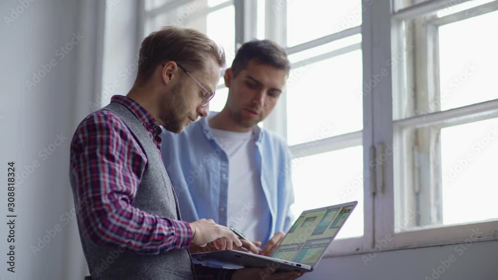 Wall mural waist up of two young web designers standing by window at office and discussing app interface sample