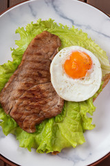 Fried egg and steak on bread for breakfast on plate and rustic table