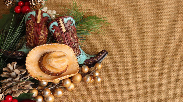 blue and brown cowboy boots and hat with pine, pine cones and berries on a tan textured background with copy space