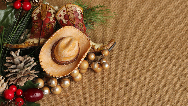 tan and brown cowboy boots and hat with pine, pine cone and berries on a tan textured background with copy space