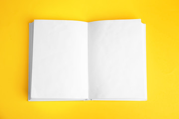 Open book with blank pages on yellow background, top view