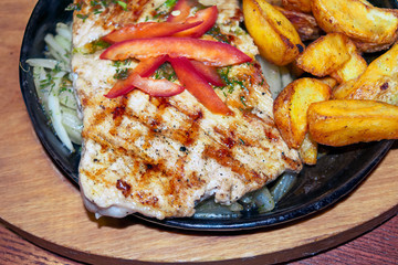 Pork steak on a cast-iron brazier. Large pork steak with fried potatoes in a cast iron pan on a...