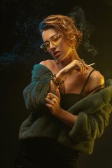 A young beautiful girl in glasses and a fur coat smokes a cigarette.