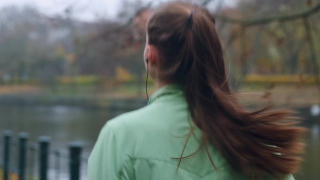Back view of sporty girl in earphones running in autumn city park