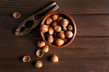 Bowl with tasty hazelnuts on wooden background