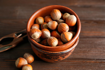 Bowl with tasty hazelnuts on wooden background