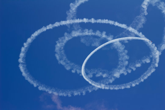 Abstract view of the vapor trail of an airplane skywriting in spiraling circles against a deep blue sky