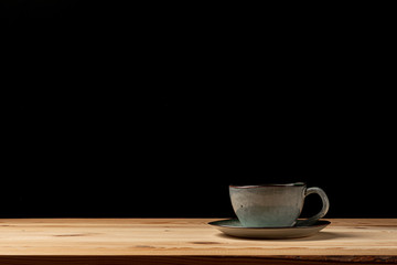 Handmade cup with coffee on the table. Countertop made of wood. Coffee beans. Black background.