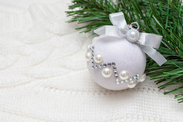 Fototapeta na wymiar A branch of fir pine tree and shiny decorative christmas ball on cozy white knitted background with copy space