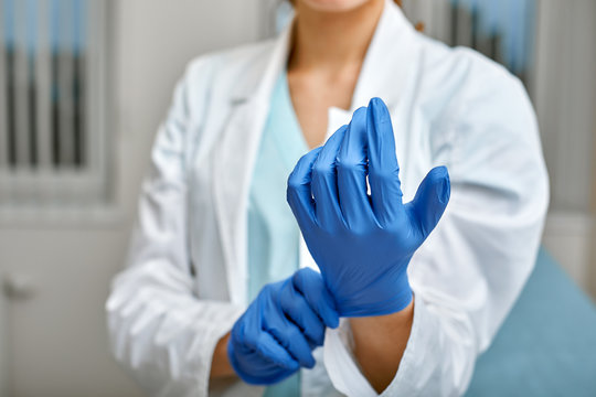 Close up of a female doctor putting a blue latex gloves on a clinic background.