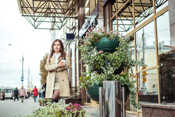 young woman drinking coffee at city street. A girl runs out of the bank, hurries in a big city. on the streets of a metropolis in autumn or early spring.