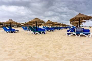 Rows of straw parasols and sunloungers on the beach at Manta Rota, Algarve, Portugal.