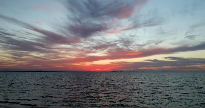 A colorful sunrise paints a cloudy sky with color over San Carlos Bay with Fort Myers Beach, Florida on the horizon in this seamless motion background video loop