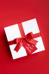 Christmas gift box with red ribbon and a bow from secret Santa on the red background