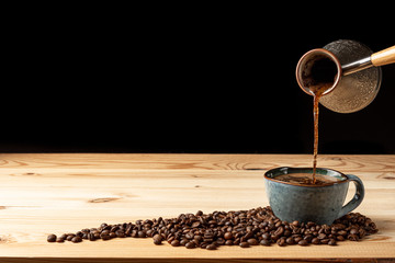 Handmade cup with coffee on the table. Countertop made of wood. Coffee beans. Black background.