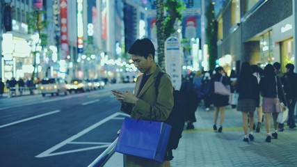 Young man surfing the internet for travel and shopping at night near bus stop