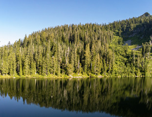 Secluded Kelcema Lake and the surrounding mountain and trees reflecting in the shaded water on a clear summer afternoon in the Mount Baker-Snoqualmie National Forest in Silverton Washington State