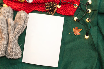 Christmas mockup, with a postcard, wishes, letter on the blanket with a kettle, leaf, tea, cone, chocolate and xmas tree lights.  Background top view blank space for text.