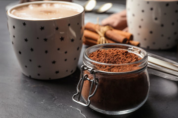 Jar with cocoa powder and cup of hot drink on grey table
