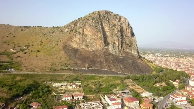 Partinico mountain rock formation with community village houses at base of mountain. Aerial orbit left view across Sicily landscape.