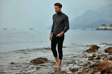 Fototapeta na wymiar Handsome man wear fashionable clothes, walking on the beach and soaking his feet