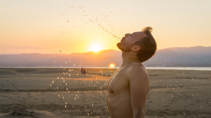 young boy pouring water from his mouth on the beach at sunset © Sergio