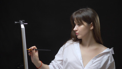 Fototapeta premium cute girl artist paints a picture on canvas with oil paints. black background